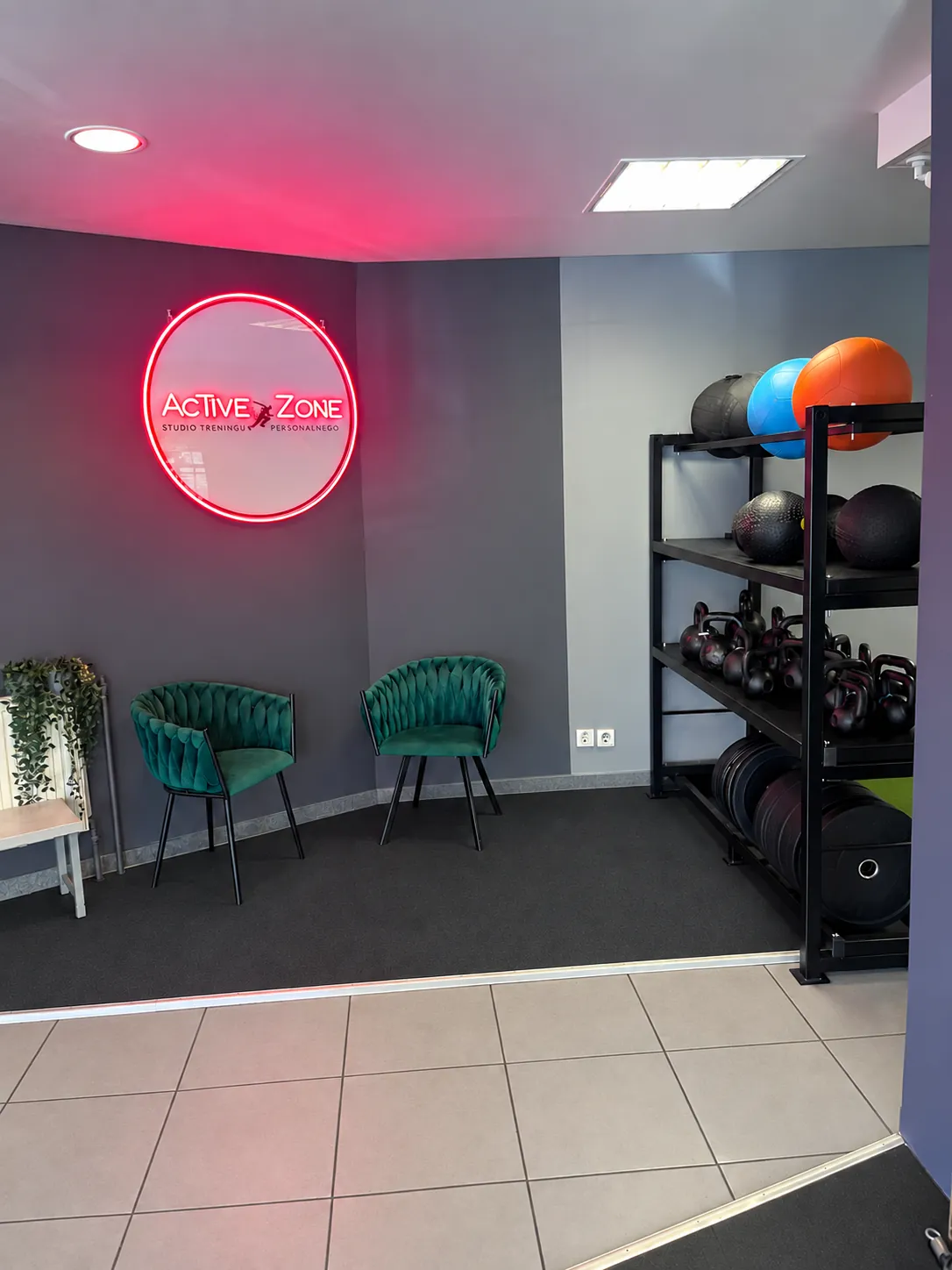Wejście do studia Active Zone: podświetlane logo na ścianie, zielone fotele i regał z piłkami oraz kettlebellami