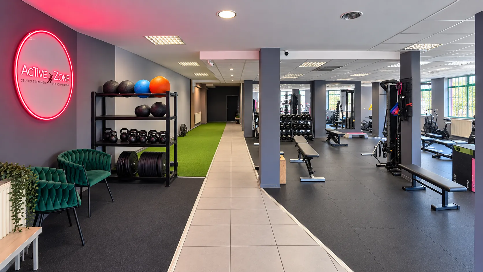 Sala Active Zone od wejścia: podświetlane logo, regał z piłkami i kettlebellami, tor ze sztuczną trawą i strefa maszyn